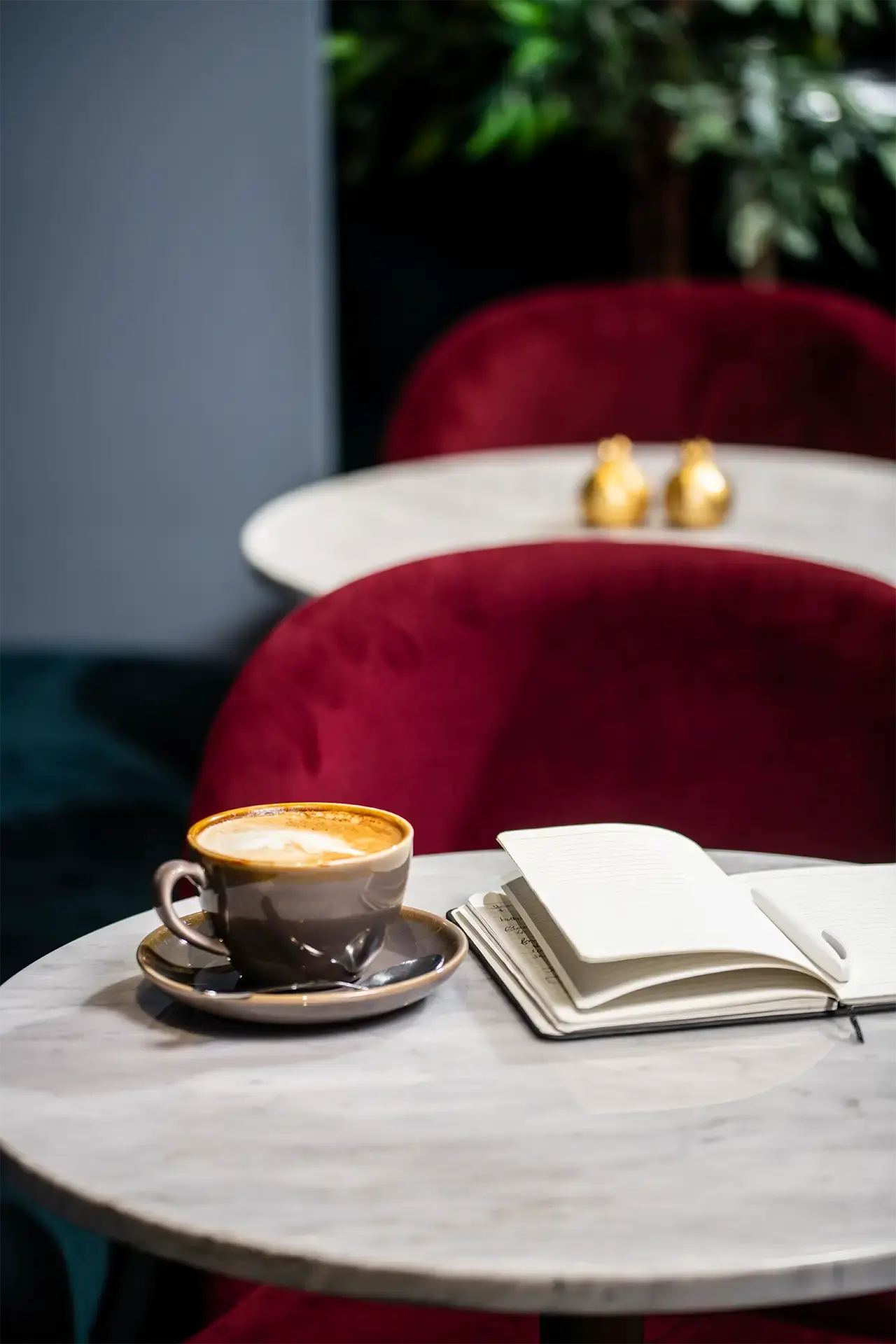 Coffee cup and open notebook on a marble café table with red velvet chairs