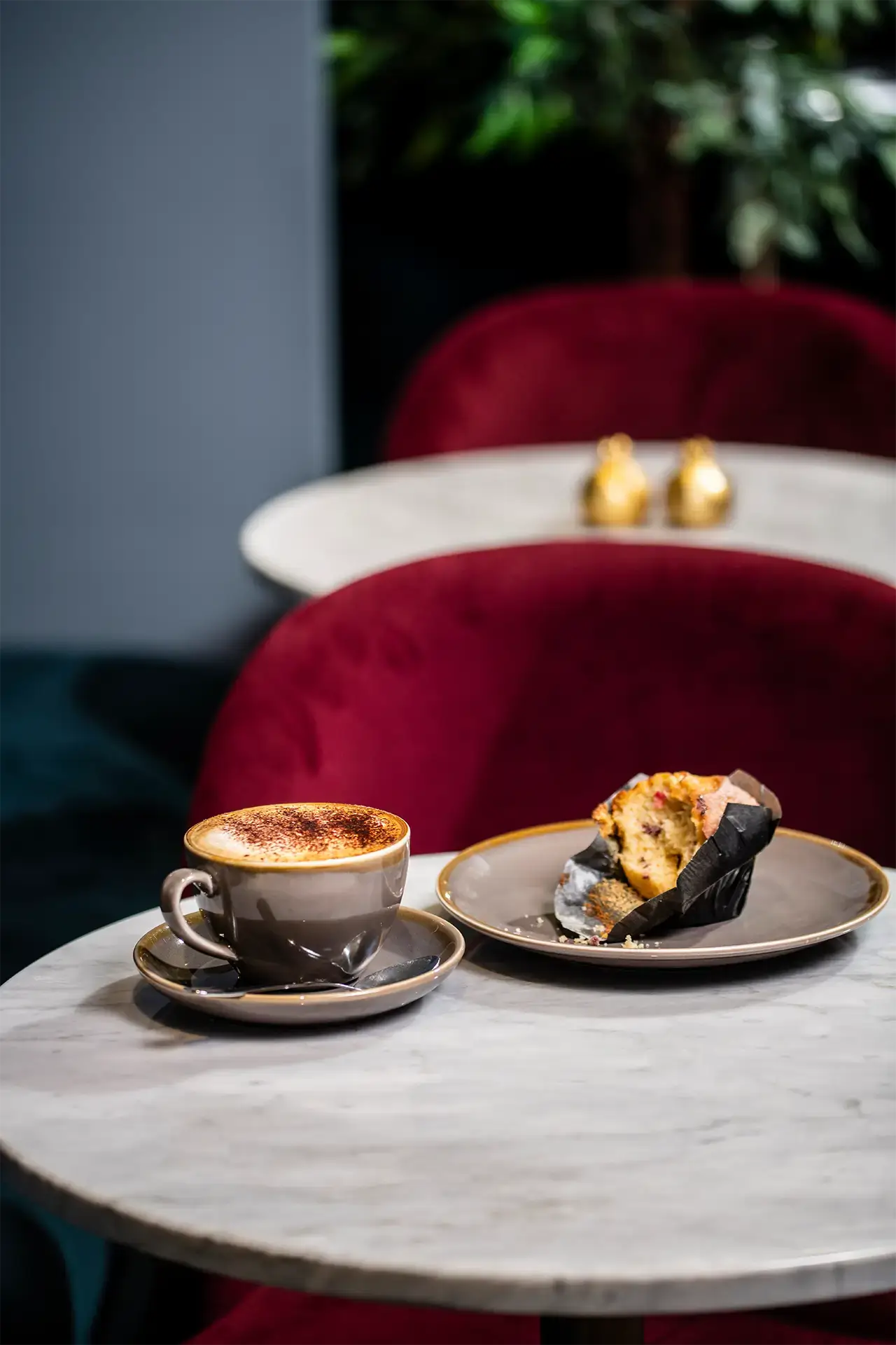 Coffee and a muffin served on a marble café table with red velvet chairs