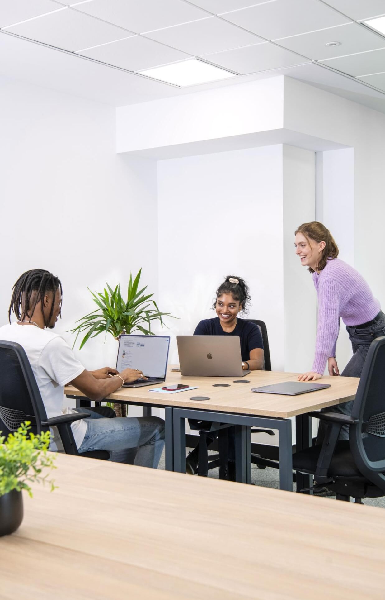 Three colleagues collaborating around a desk with laptops in a bright office