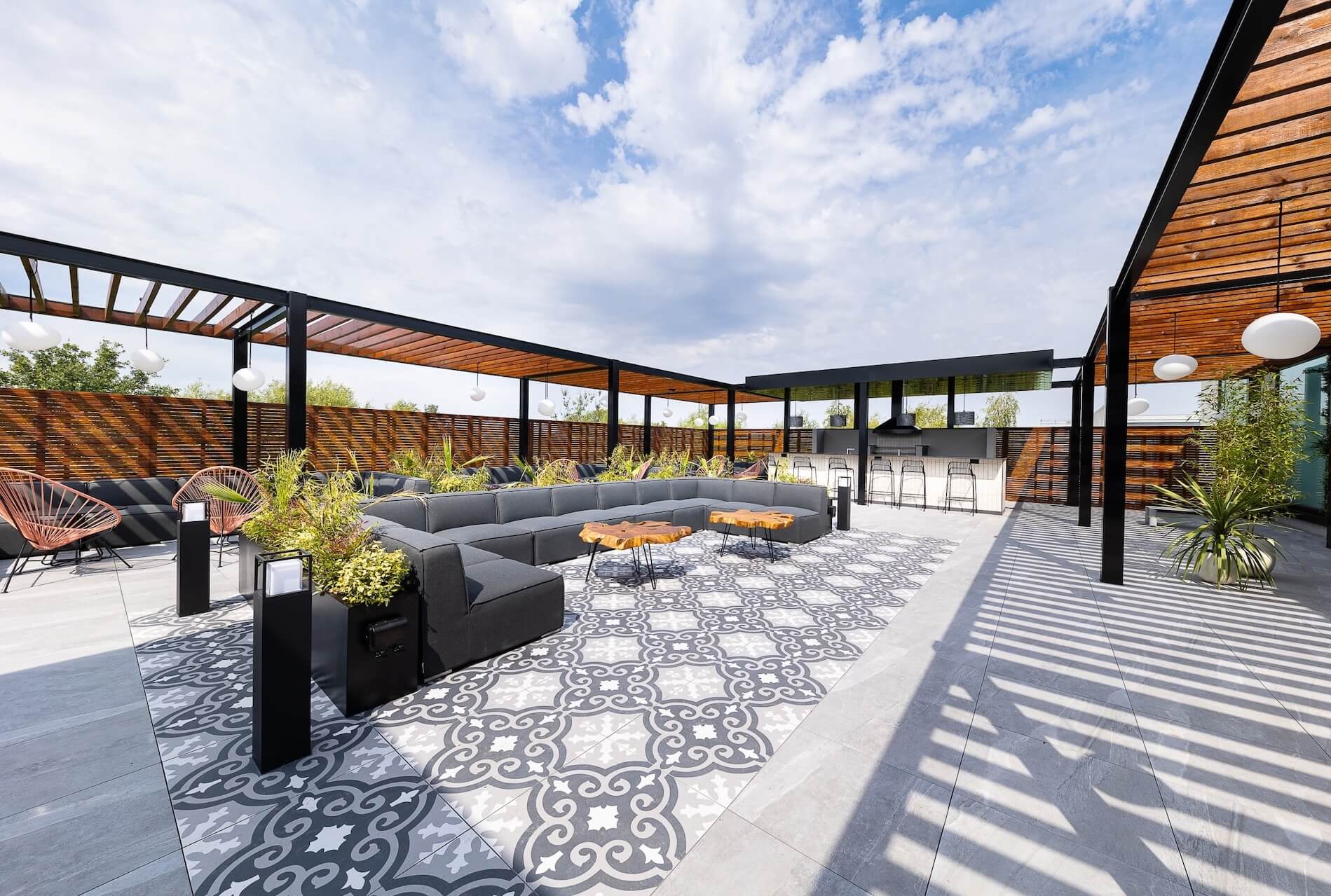 Rooftop terrace with grey corner sofas, a bar and pergolas under a blue sky