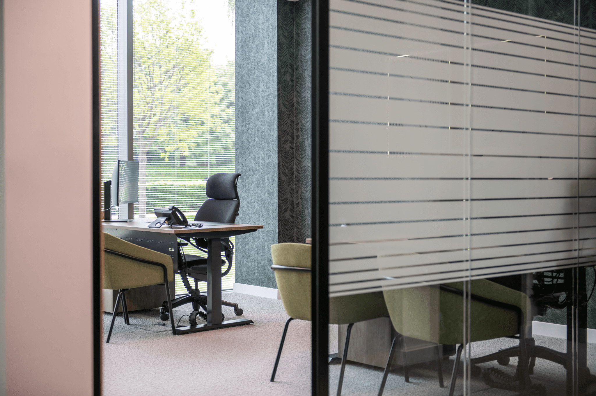 Private office with a desk, ergonomic chair and window view, seen through a frosted glass partition