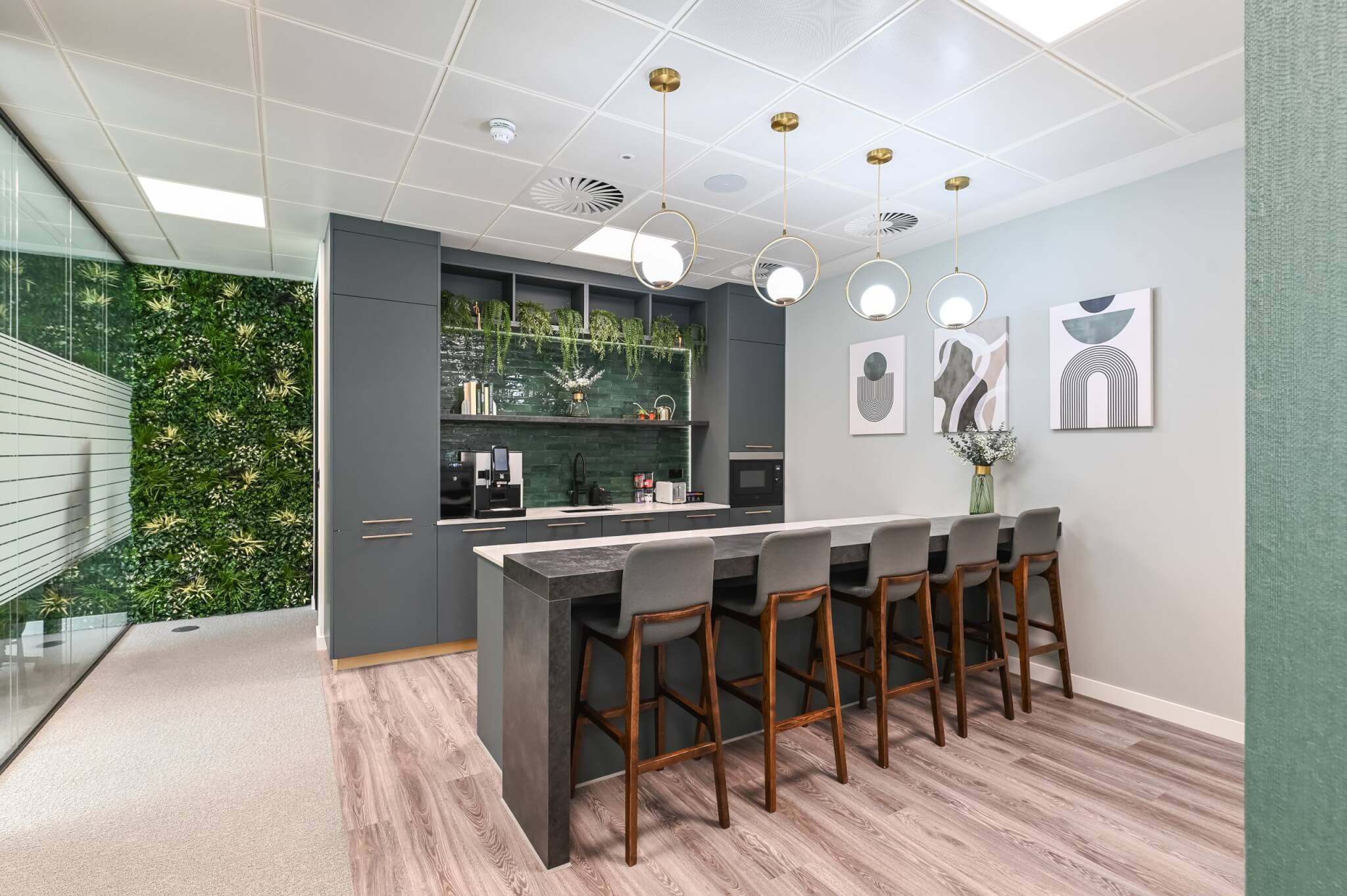 Office kitchen with a green living wall, breakfast bar stools and pendant lighting