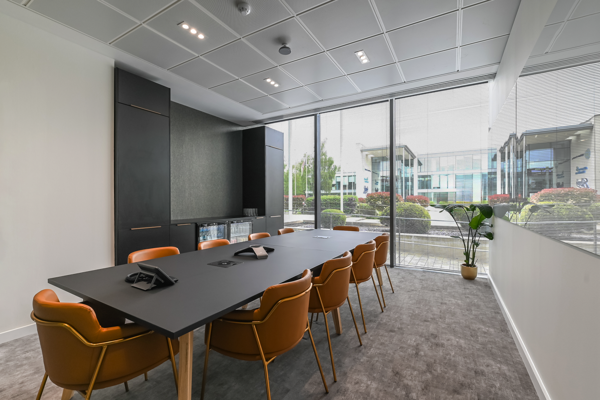Meeting room with orange chairs, black cabinetry and floor-to-ceiling windows overlooking the car park