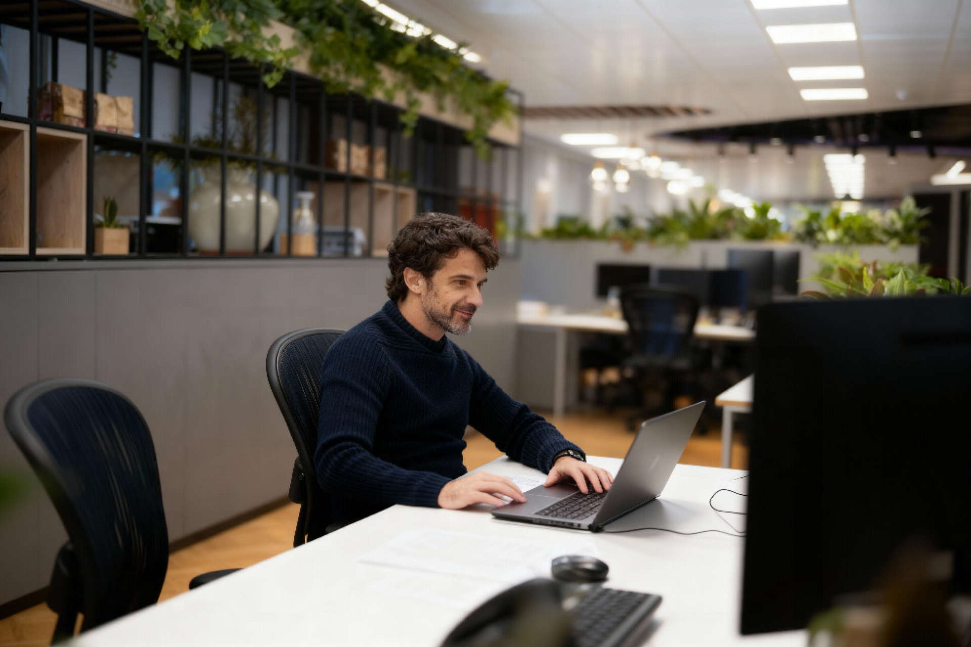 Man working on a laptop at a desk in a plant-filled coworking office