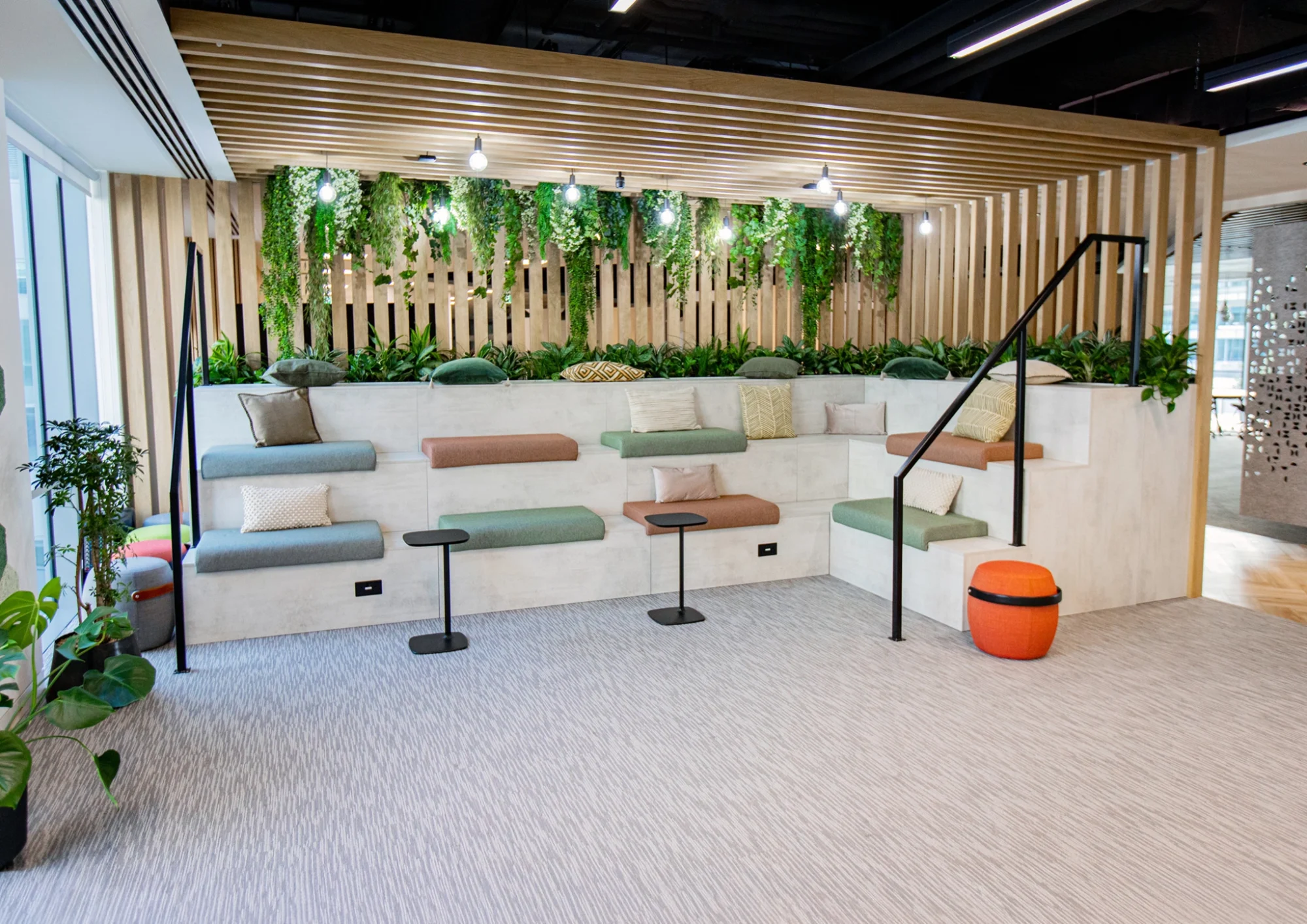 Tiered lounge seating with colourful cushions beneath a hanging plant wall