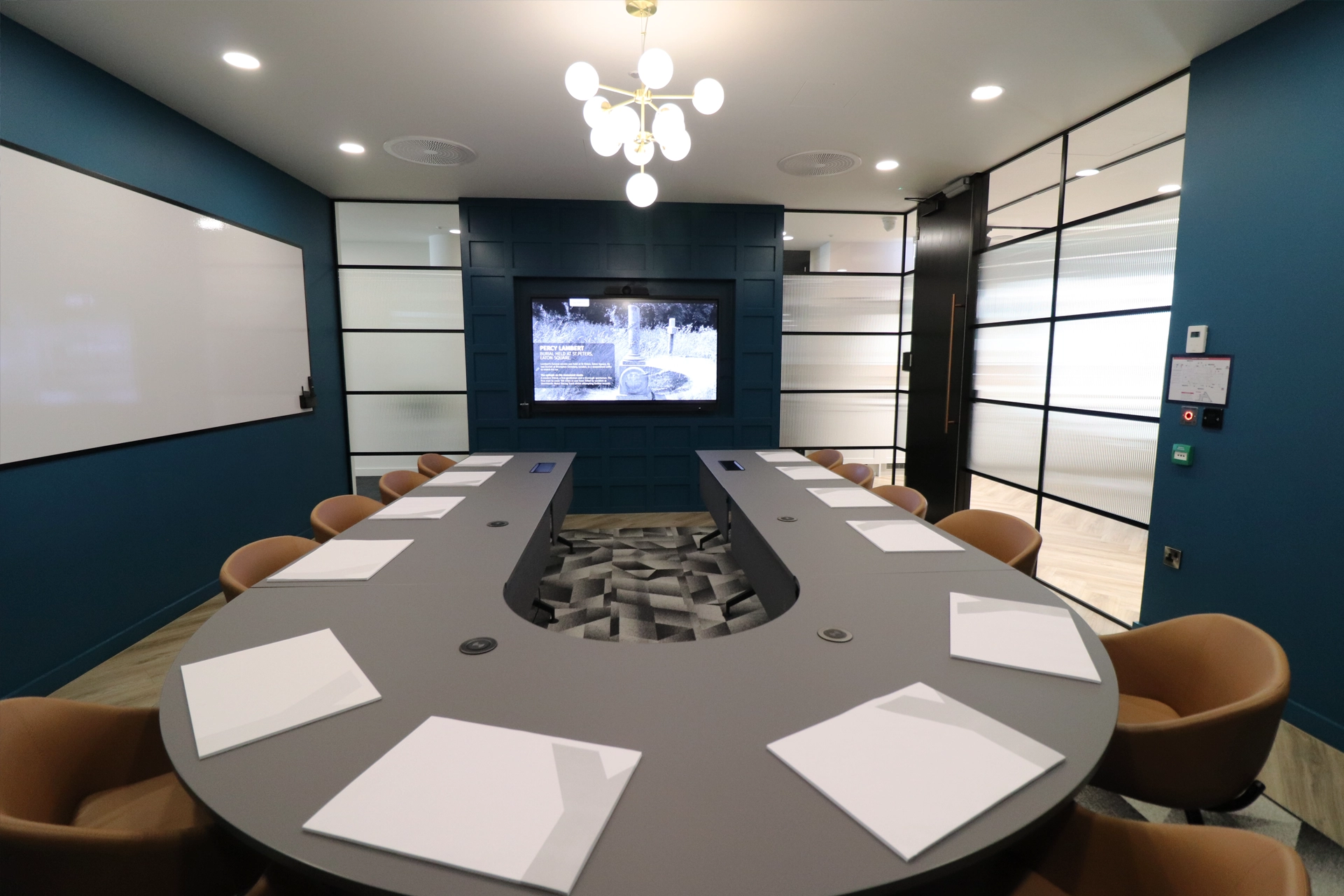 The Lambert Suite meeting room with a U-shaped table, teal panelled wall and screen