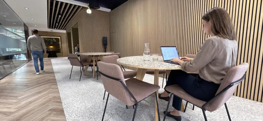 Woman working on a laptop at a wooden table in a wood-panelled breakout area